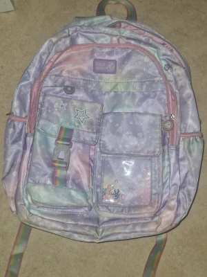 Ryggsäck - Säljer en superfin ryggsäck i pastellfärger från Glo Anfu. Väskan har regnbågsfärgade detaljer, flera fack med stjärn- och hjärtmönster samt reflexdetaljer på axelbanden. 2 stora fask varav en har små fickor i sej. 2 små fickor på framsidan samt 2 fack på vardera sida tillför flaska. Någor smutsig- går att göra rent men tiden finns inte föe mej. Perfekt för dig som gillar färgglada accessoarer och vill sticka ut.