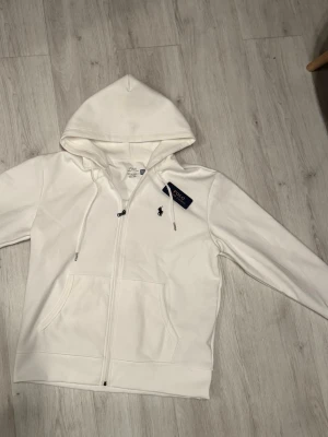 Polo Ralph Lauren zip hoodie kofta - Snygg vit hoodie från Polo Ralph Lauren med dragkedja framtill. Aldrig kommit till användning. Helt ny