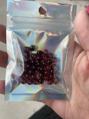 Mörkröda glaspärlor i påse - Säljer ett paket med mörkröda, runda glaspärlor perfekta för att skapa egna smycken som armband, halsband eller örhängen. Pärlorna kommer i en holografisk zip-påse och har en djup vinröd färg som ger en lyxig känsla till sopiga DIY-projekt.