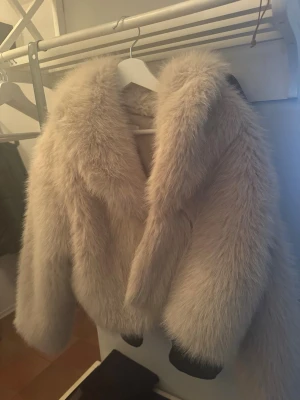Beige fluffig pälsjacka Zara ny oanvänd - Supersnygg beige pälsjacka med bred krage och oversized passform. Jackan har långa ärmar och är gjord i ett mjukt, fluffigt material som ger en lyxig känsla. Perfekt för att hålla värmen under kalla dagar och ger en trendig look. Kostade 1300