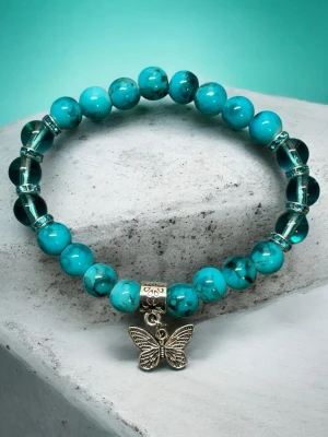 Turkost pärlarmband med fjärilshänge - Snyggt armband med turkosa pärlor och några mörkare glaspärlor, dekorerat med små silverfärgade detaljer. Armbandet har ett fint fjärilshänge i metall som ger en unik touch. Perfekt accessoar för dig som gillar boho-stil och färgglada smycken.