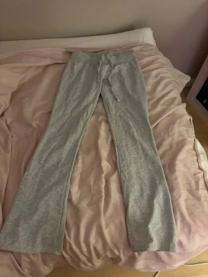 Gråa mjukisbyxor med utsvängda ben - Säljer ett par ljusgrå mjukisbyxor med utsvängda ben och dragsko i midjan. Byxorna är i mjukt och stretchigt material, perfekta för chill dagar. Inga synliga loggor eller märken. Passar dig som gillar en relaxed och bekväm stil.