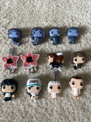 Stranger Things Funko Pop-nyckelringar -  Styckpris 20 kr per gubbe. Samling med 12 stycken Stranger Things Funko Pop-nyckelringar i plast. Figurerna är färgglada och föreställer olika karaktärer och monster från serien, inklusive två Demogorgon och flera huvudpersoner. Perfekt för fans av serien som vill ha unika samlarprylar.
