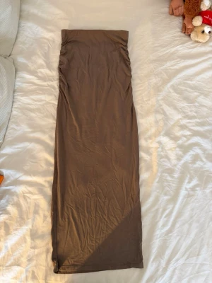 Brun långkjol i mjukt material - Säljer en enkel och stilren brun långkjol i mjukt, stretchigt material. Kjolen har rak passform nertill och en scrunch upptill. Från Gina Tricot storlek 34