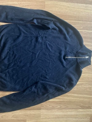 Mörkblå stickad tröja Jack & Jones - Mörkblå stickad tröja från Jack & Jones med halv dragkedja vid halsen och hög krage. Tröjan har lång ärm och är tillverkad i mjukt material som passar perfekt till kyligare dagar.