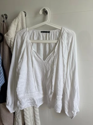 Vit blus med spetsdetaljer - Luftig vit blus med v-ringning och långa ärmar. Blusen har fina spetsdetaljer vid ärmslut och nederkant samt en lätt skrynklig struktur i tyget. Perfekt för en avslappnad och trendig look.
