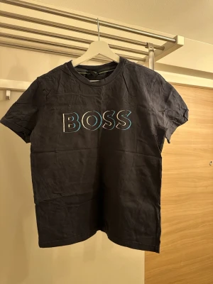 Marinblå BOSS t-shirt med tryck - Snygg marinblå t-shirt från BOSS med stort färgglatt BOSS-tryck på bröstet. Klassisk rund halsringning och korta ärmar. Tillverkad i mjuk bomull som känns skön mot huden. Perfekt för en avslappnad och stilren look.