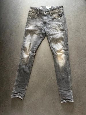 Grå skinny jeans från Replay - Snygga grå skinny jeans från Replay med slitna detaljer och tvättad look. Klassisk femficksmodell med Replay-logga på myntfickan. Jeansen har smal passform och är tillverkade i bomull med stretch för extra komfort. 28/30