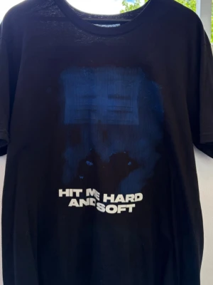 Svart t-shirt med blått tryck - Svart Billie Eilish t-shirt med blått grafiskt tryck och texten 'HIT ME HARD AND SOFT' på framsidan. Klassisk rund hals och korta ärmar. Den är aldrig använd! 
