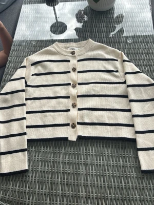 Randig beige kofta från Zara - Trendig beige kofta från Zara med svarta horisontella ränder och snygga mönstrade knappar framtill. Koftan är aldrig använd endast provad. 