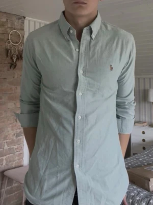 Ljusblå skjorta Ralph Lauren - Klassisk ljusblå skjorta från Ralph Lauren med button-down krage och broderad logga på bröstet. Skjortan har lång ärm, vita knappar och är tillverkad i bomull. Perfekt för en clean och stilren look. Storlek L men passar också M 