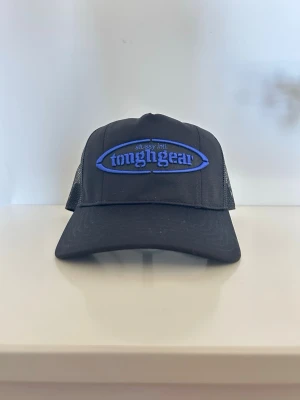 Svart Stussy truckerkeps tough gear - Säljer min svarta truckerkeps från Stussy med blå broderad 'tough gear'-logga framtill. Kepsen har böjd skärm och mesh på sidorna och bak för extra ventilation. Justerbar passform med snapback. Perfekt för en streetwear-look.
