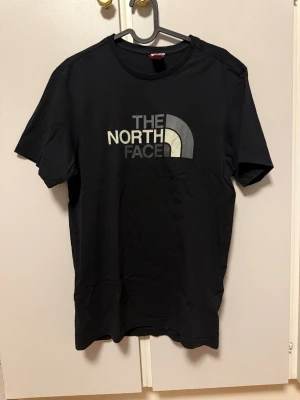 The North Face t-shirt - Snygg svart t-shirt från The North Face med klassisk logga i vitt och grått på bröstet. T-shirten har rund halsringning och korta ärmar. Tillverkad i mjuk bomull som känns skön mot huden. Perfekt för en avslappnad och stilren look.