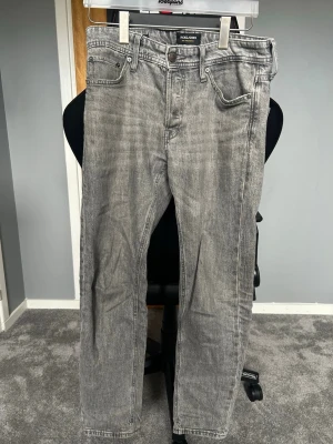 Grå jeans från Jack & Jones - Säljer ett par grå jeans från Jack & Jones med klassisk femficksmodell och raka ben. Jeansen har en snygg tvättad look. Storlek: 28/30 NYPRIS:599kr Pris kan diskuteras