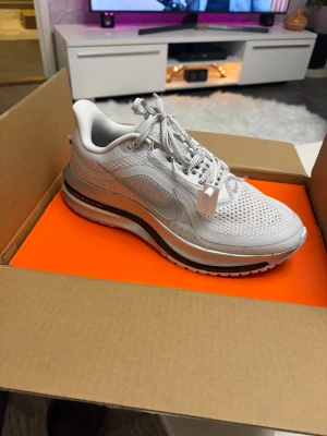 Nike vita sneakers med meshdetaljer - Snygga vita Nike sneakers med mesh på ovandelen för extra andningsförmåga. Skon har en tydlig swoosh-logga på sidan, reflekterande detaljer och en tjock, dämpad sula med svart och grå inslag. Perfekt för dig som gillar sportig och clean stil.