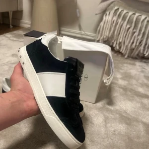 Valentino Garavani Sneakers/Skor Svarta - Snygga svarta sneakers från Valentino Garavani med vit sidopanel och vit sula. Skorna har svarta skosnören, detaljer i mocka och läder samt logga på plösen. Perfekta för dig som gillar exklusiv och stilren design. Bra skick och väl skötta, 9/10 i betyg och inga defekter.