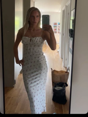 Vit långklänning med blommigt mönster - Säljer en vit långklänning med små blommor i rosa och rött. Klänningen har smala axelband, söt snörning framtill och en figurnära passform. Perfekt för sommarens alla tillfällen! Den är från Gina tricot men den säljs inte längre. Storlek xxs men passar mig som vanligt vis är xs. Använd en gång