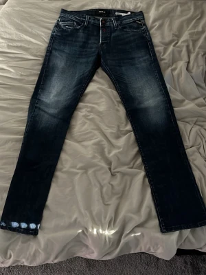 Mörkblå slim fit jeans Replay - Snygga mörkblå slim fit jeans från Replay med lätt slitna detaljer och klassisk femficksdesign. Jeansen har en diskret tvättad look och raka ben. Perfekta för dig som gillar en modern och stilren stil.