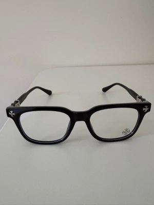 Svarta chrome hearts glasögon med silver detaljer  - Snygga svarta solglasögon med rektangulär form och coola silverfärgade stjärndetaljer vid hörnen. Bågarna är i plast och ger en modern vibe som passar till de flesta outfits. Perfekta för dig som vill sticka ut lite extra.