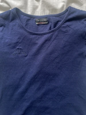 Marinblå t-shirt från Kappa - Snygg marinblå t-shirt från Kappa med broderad logga på bröstet. Klassisk rund halsringning och korta ärmar. Tillverkad i mjuk bomull som är skön att ha på sig hela dagen.