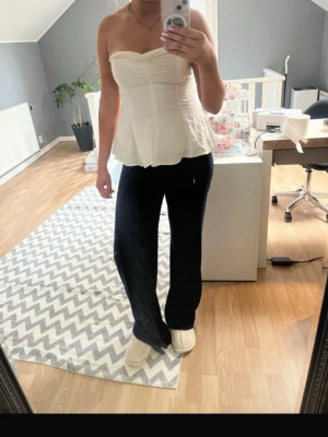 Vit axelbandslös korsett-topp - Snygg vit axelbandslös korsett-topp med hjärtformad urringning och lätt utsvängd nederkant. Perfekt att styla med jeans eller kjol för en trendig look. Toppens material känns mjukt och följsamt.