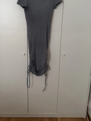 Ljus blå ribbad klänning med snörning - Snygg ljus blå ribbad klänning med korta ärmar och trendig snörning i sidorna nedtill. Klänningen har en kroppsnära passform och är tillverkad i ett stretchigt material som ger en bekväm känsla. Perfekt för dig som gillar en enkel men stilren look.