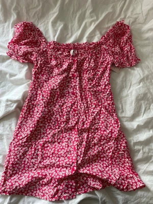 Rosa off-shoulder klänning  - Kort rosa klänning, off-shoulder puffärm och knappar framtill. I storlek 38 från Nelly. Aldrig andvänd, lapp kvar 