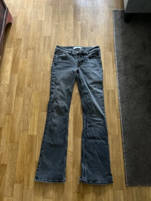 Grå bootcut jeans med rå kant - Snygga grå bootcut jeans med råa kanter nertill och klassiska fem fickor. Jeansen har låg midja och är tillverkade i ett mjukt denimtyg. Perfekta för en avslappnad och trendig look.