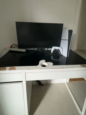 Sony PlayStation 5 vit konsol - Säljer en PlayStation 5 konsol i vit och svart design från Sony. Konsolen har en futuristisk form och står upprätt bredvid en matchande DualSense-handkontroll. Perfekt för gaming och underhållning.