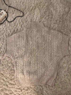 Beige kabelstickad väst med polokrage - Säljer en beige kabelstickad väst med polokrage och korta ärmar. Aldrig använd och har inga defekter. Super skön och sitter fint! Skriv vid fler frågor eller bilder