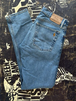 Blå jeans från Polo Ralph Lauren - Klassiska blå jeans från Polo Ralph Lauren med rak passform och femficksdesign. Jeansen har en läderpatch med logga bak i midjan och den ikoniska broderade polospelaren på bakfickan. Tillverkade i bomull för en skön och tidlös look.