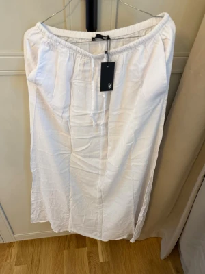 Helt ny vit långkjol från Lager 157 - Vit långkjol från Lager 157 med resår i midjan och enkel, rak passform. Kjolen är gjord i ett lätt och luftigt material som passar perfekt till varmare dagar. Stilren design utan mönster eller extra detaljer.