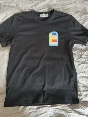 Svart Casa Blanca t-shirt med tryck - Snygg svart t-shirt från Casa Blanca med färgglatt grafiskt tryck fram och stort tryck på ryggen. T-shirten har rund hals och korta ärmar. Materialet känns mjukt och skönt, troligen bomull. Perfekt för dig som gillar streetwear och unika prints.