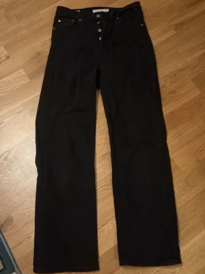 Svarta Levi's Premium straight jeans - Säljer ett par svarta Levi's Premium jeans i modellen Ribcage Straight. Jeansen har raka ben, hög midja och klassisk knappgylf. Snygga detaljer med silverknappar och kopparnitar. Perfekta för en clean och stilren look.