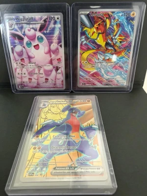 Pokémonkort Wigglytuff, Zeraora, Garchomp - Tre Pokémonkort: Wigglytuff i rosa med glittrig bakgrund, Zeraora i färgstark design med eltema och Garchomp EX med guldfärgad ram och holografisk effekt. Alla korten är i plastfickor och har unika illustrationer och attacker. Perfekt för samlare eller Pokémonfans.