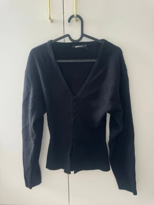 Svart kofta med knappar från Gina Tricot - En svart, långärmad kofta från Gina Tricot med v-ringning och knappar framtill. Koftan har en smickrande passform och är perfekt att styla över ett linne eller t-shirt. Enkel och stilren design som funkar till det mesta.