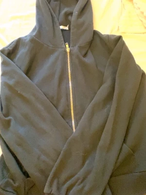 Svart hoodie med dragkedja - En klassisk svart hoodie med dragkedja framtill och huva. Hoodien har långa ärmar och ribbade muddar vid ärmslut och nederkant. Perfekt för en avslappnad stil och enkel att matcha med andra plagg.