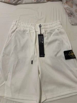 Vita shorts från Stone Island - Snygga vita shorts från Stone Island med elastisk midja och snörning. Shortsen har två sidofickor och den klassiska Stone Island-loggan på vänster ben. Perfekta för sommaren och riktigt sköna att bära.