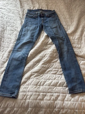 Blå nudie jeans - Snygga blå jeans med rak passform och klassisk tvätt. Jeansen har fem fickor, bälteshällor och subtila slitningar för en avslappnad look. Tillverkade i bomull med en lätt stretch för extra komfort. Perfekta till en avslappnad stil.