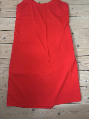 Röd ärmlös klänning - En enkel och stilren röd klänning med rak passform och ärmlös design. Har inte fått användning för den. Köpt second hand. 
