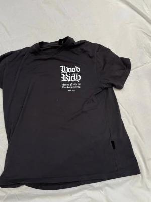 Svart Hoodrich t-shirt med tryck - Cool svart t-shirt från Hoodrich med vit text och grafiskt tryck både fram och bak. T-shirten har normal passform, rund hals och är tillverkad i mjuk bomull. Perfekt för dig som gillar streetwear och vill sticka ut med snygga detaljer. ❗️tröjan är oversize och är passar som  L❗️