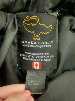 Svart dunjacka från Canada Goose - Säljer en svart dunjacka från Canada Goose med stor huva och klassisk logga på ärmen. Jackan har flera fickor framtill och är perfekt för kalla vinterdagar  och fodrad med dun för extra värme. 