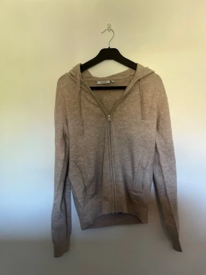 Beige stickad/casmir hoodie med dragkedja - Mysig beige stickad hoodie från Filippa K med dragkedja framtill och två fickor. Tröjan har huva med dragsko och ribbade muddar vid ärmslut och nederkant. Perfekt för lager på lager och chill stil.