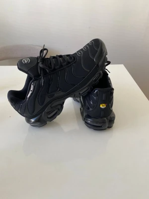 Nike Air Max Tn  Plus helsvarta sneakers - Säljer ett par helsvarta Nike Air Max Plus sneakers med ikoniska vågmönster och Tn-detalj på hälen. Skorna har en chunky sula med synlig Air-enhet och är tillverkade i mesh och syntetmaterial. Perfekta för dig som gillar streetwear och vill ha en clean look.