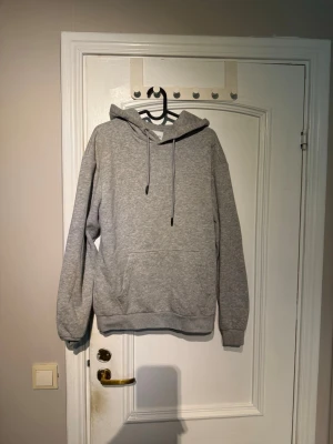 Grå hoodie från Jack & Jones - Säljer en klassisk grå hoodie från Jack & Jones med huva och dragsnören. Hoodien har en stor magficka och ribbade muddar vid ärmslut och nederkant. Tillverkad i mjukt bomullsmaterial som är skönt att ha på sig.