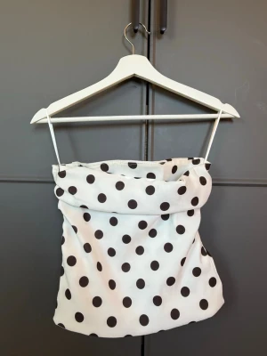 Vit prickig tub linnetopp  - Supersöt vit linnetopp med svarta prickar. Toppen har en lätt draperad passform och är perfekt för en trendig och lekfull look. Materialet känns svalt och mjukt mot huden, och den är enkel att matcha med både jeans och kjol💖🌸🌸🖤🤍