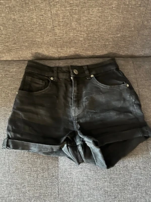 Svarta högmidjade jeansshorts - Snygga svarta högmidjade jeansshorts med uppvikta benslut och klassisk femficksdesign. Perfekta till sommaren och lätta att matcha med olika stilar. Stängs med knapp och dragkedja framtill. Provats nån gång men aldrig riktigt använt bara legat i garderoben 