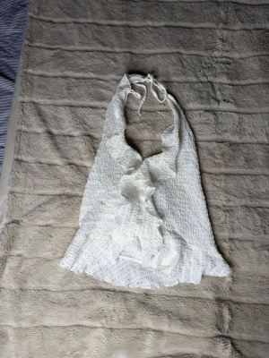 Vit omlott halterneck topp med volang - Supersöt vit halterneck topp med omlott och volangdetaljer framtill. Toppen har knyt i nacken och är alltså justerbar. Volang effekten fram ger en otrolig sommar/v-cay känsla, toppen kommer från Nelly och är i storlek S. Nyskick💞