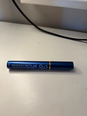 SKINSECRETLAB ögonfransserum blå - Ögonfransserum från SKINSECRETLAB i en stilren blå tub med gulddetalj. Förpackningen är smal och cylinderformad, perfekt att ha i necessären. Designen är modern med vit text och en molekylgrafik på sidan.