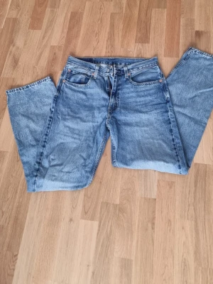 Blå raka jeans från Levi's 31/34 - Klassiska blå jeans från Levi's med rak passform och fem fickor. Jeansen har en tidlös tvätt och är tillverkade i slitstarkt denim med metallknappar och nitar. Perfekta för en avslappnad och trendig look.